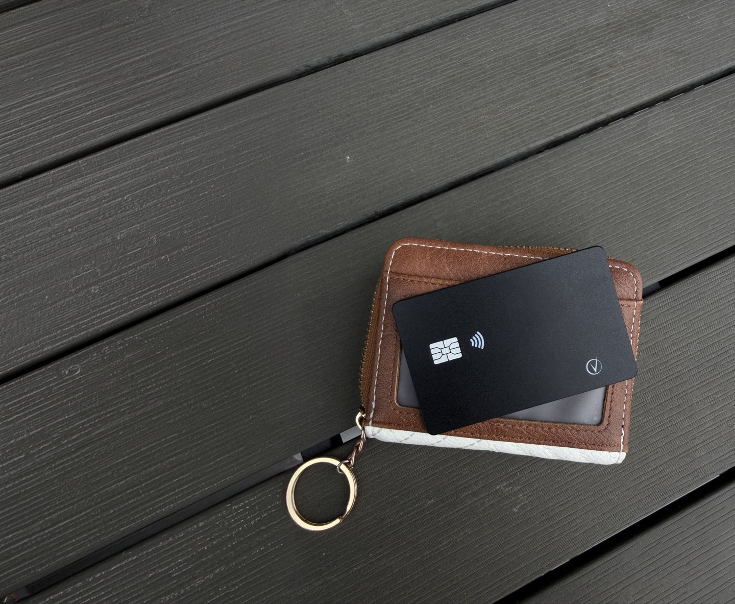 Black Vantamo tracker card slipped into the slot of a small brown wallet on a dark wooden table