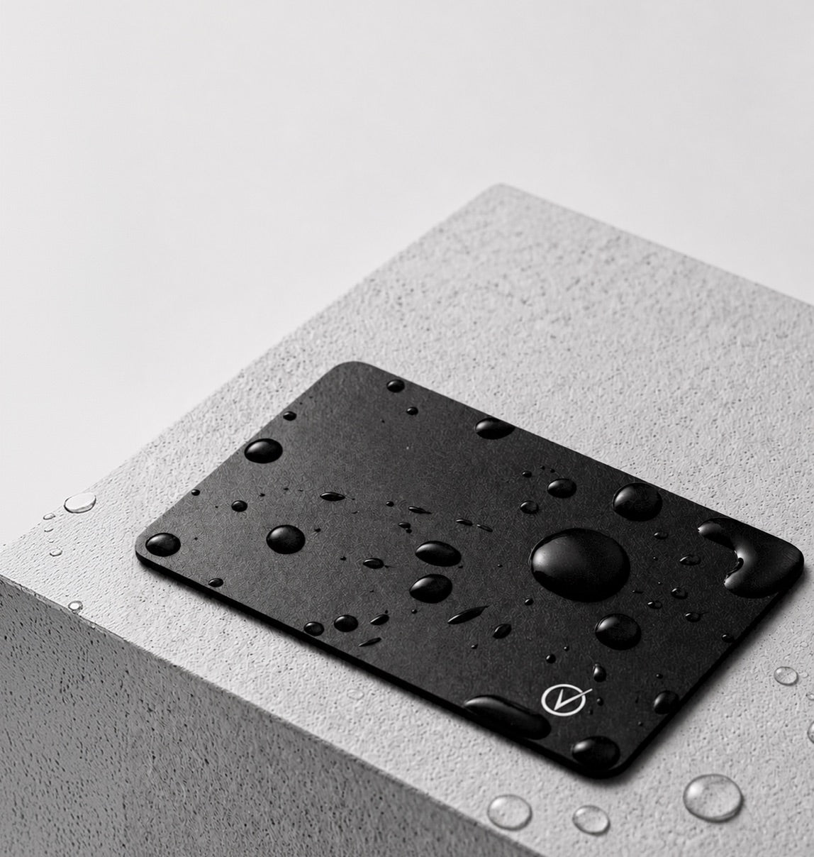 Black Vantamo tracker card covered in water droplets resting on a concrete block
